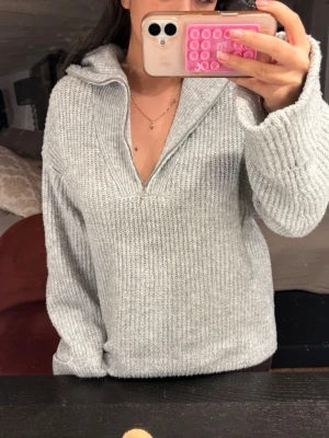 Grå stickad tröja med half zip - Mysig grå stickad tröja med halv dragkedja och krage. Tröjan har en relaxed passform och långa ärmar, perfekt för kyliga dagar. Enkel att styla och superbekväm att bära.