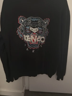 Svart Kenzo tröja. Storlek S. Helt ny. Pris; 799kr - Svart sweatshirt från Kenzo i storlek S med ikoniskt broderat tigerhuvud i blått, vitt och rött framtill. Tröjan har rund halsringning och långa ärmar. Perfekt statement-plagg för dig som gillar streetwear och vill sticka ut.