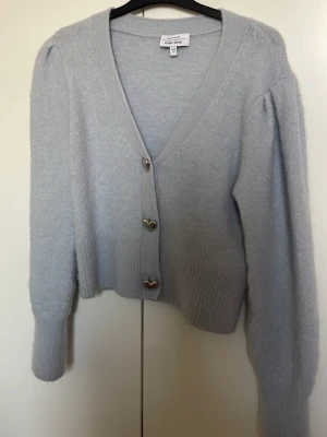 Ljusblå kofta från & Other Stories - Supersöt ljusblå kofta från & Other Stories med fluffig känsla och tre silvriga hjärtformade knappar. Koftan har v-ringning, långa ärmar med lätt puff och ribbade muddar. Perfekt för lager på lager under kyliga dagar.