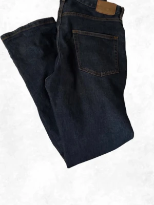 Mörkblå jeans från Jeanerica - Säljer ett par klassiska mörkblå jeans från Jeanerica. Jeansen har raka ben, fem fickor och kontrastsömmar i orange. 