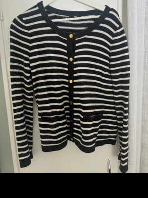 Randig svartvit kofta från H&M - Säljer en svartvit randig kofta från H&M i storlek M. Koftan har guldknappar framtill, i Bomull