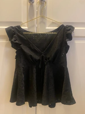 Svart blus med volang och knyt - Supersöt svart blus med v-ringning, knyt framtill och volangärmar.