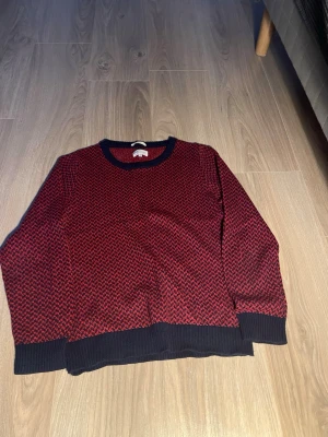 Röd och svart stickad tröja GANT - Säljer en röd och svart stickad tröja från GANT med småmönstrad design. Tröjan har rund halsringning och ribbade muddar vid ärmslut och nederkant. Perfekt för dig som vill ha en klassisk men ändå unik look.