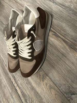 Philippe Model sneakers brun/vit - Snygga sneakers från Philippe Model i beige och brunt med vita detaljer. Skön nu till våren som inte används. Rikigt bra skick förutom en defekt på högra häl, de sista bild, har limmat ihop sprickan o funkar som vanligt