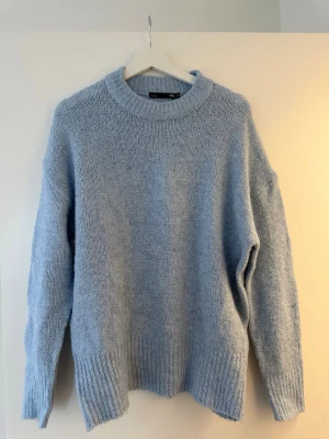 Ljusblå stickad tröja från 157 - Mysig ljusblå stickad tröja från 157 med rund halsringning och breda ribbade muddar vid ärmslut och nederkant. Perfekt för kyliga dagar och enkel att styla med jeans eller kjol. Är mer som storlek S-M.