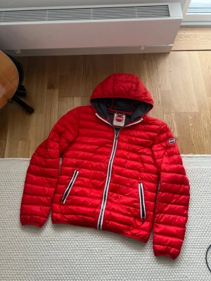 Röd Colmar pufferjacka med huva - Säljer en röd pufferjacka från Colmar med huva och vita dragkedjor. Jackan har två fickor framtill och Colmar-logga på ärmen. Insidan är mörkgrå och materialet är lätt och syntetiskt, perfekt för kyliga dagar.PRISET ÄR FAST