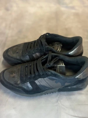 Valentino Rockrunner sneakers svart camo - Snygga Valentino Rockrunner sneakers i svart med camouflagemönster. Skorna har svarta snören, detaljer i mocka och skinn samt en cool platt sula. Perfekta för dig som vill ha en unik och trendig look.