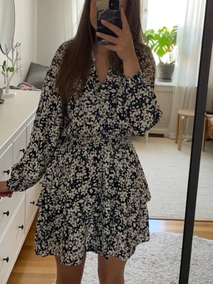 Blommig volangklänning - En jättesöt klänning med marinblått och vitt blommönster. Holly & Whyte. Storlek S. Klänningen har v-ringning, långa ärmar, markerad midja med smock och volanger i kjolen. Mycket bra skick! Klänningen är helt ny med prislapp kvar. Perfekt för sommaren! Kontakta vid frågor💕