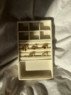 Beige smyckesförvaring i sammet - Praktisk smyckesförvaring i beige sammet med flera fack och rader för ringar, örhängen eller andra småsmycken. Rektangulär form och mjuk yta som skyddar dina accessoarer. Perfekt att ha på nattduksbordet eller i garderoben.