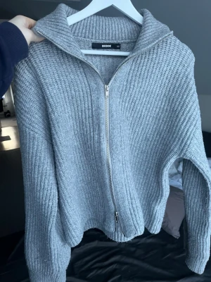 Grå ribbad ziptröja från Bik Bok - Mysig grå ribbstickad tröja från Bik Bok med dragkedja framtill och hög krage. Tröjan har långa ärmar och en avslappnad passform, perfekt för lager på lager. Materialet känns mjukt och stretchigt, vilket gör den superbekväm att bära.