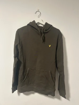 Mörkgrön hoodie från Lyle & Scott - En mörkgrön hoodie från Lyle & Scott med klassisk gul logga på bröstet. Hoodien har huva och en stor magficka framtill. Tillverkad i mjukt bomullsmaterial och har ribbade muddar vid ärmslut och nederkant. Hoodien är använd cirka tre gånger. Pris kan diskuteras. Fler bilder skickas vid behov.