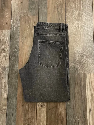Svarta raka jeans från Bershka - Säljer ett par svarta raka jeans från Bershka med klassisk femficksdesign och knappgylf. Jeansen har en tvättad look och är tillverkade i kraftig denim som ger en cool vintagekänsla. Perfekta för dig som gillar en avslappnad och trendig stil.