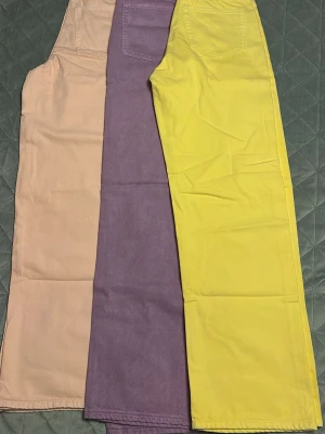 Färgade raka jeans från Stay - Tre par raka jeans från Stay i trendiga färger: ljusrosa, lila och gul. Jeansen har klassisk femficksdesign och är tillverkade i bomullstyg med en mjuk känsla. Perfekta för dig som vill sticka ut med färg och ha en relaxed vibe.