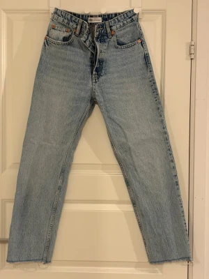 Ljusblå raka jeans från Zara - Ljusblå jeans från Zara med rak passform och hög midja. Klassisk femficksmodell med gylf och knapp. Jeansen har råa, avklippta benslut för en trendig look. Tillverkade i denim av bomull.