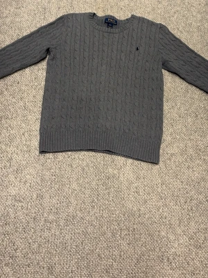 Grå tröja Polo Ralph Lauren - Snygg grå  tröja från Polo Ralph Lauren.  Helt oanvänd fick den i julklapp men har inte använt den och den var för liten för mig. Tröjan har rund halsringning och klassiskt stickat mönster. Perfekt för dig som gillar stilrena och tidlösa plagg. 