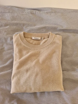 Rvls beige tröja - Snygg beige tröja från RYLS med rund halsringning och långa ärmar. Tröjan har ribbade muddar vid ärmslut och nederkant, vilket ger en clean och stilren look. Perfekt att matcha med jeans eller kjol för en enkel och trendig outfit.