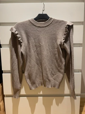 Beige stickad tröja med volang - Säljer en beige stickad tröja från Object med volangdetaljer längs axlarna. 