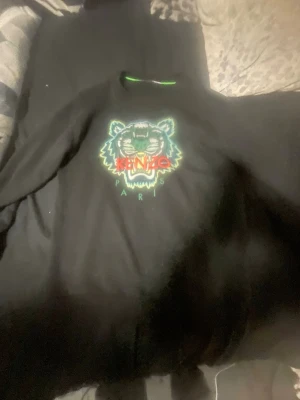 Svart sweatshirt med tiger från Kenzo - Cool svart sweatshirt från Kenzo med det ikoniska tigerhuvudet broderat i grönt, vitt och rött på bröstet. Tröjan har rund halsringning och ribbade muddar. Perfekt för dig som gillar streetwear och vill sticka ut med en klassisk logga.