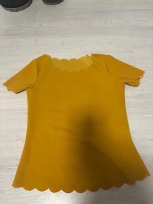 Gul topp med vågig kant Shein - Snygg gul topp med korta ärmar och unika vågiga kanter vid halsringning, ärmslut och nederkant. Toppen har en enkel, figurnära passform.