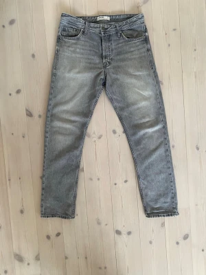 Grå Loose jeans från Jack & Jones  - Säljer ett par grå jeans från Jack & Jones med loose passform och klassisk femficksdesign. Jeansen har en snygg tvättad look och är tillverkade i denim. Perfekta för en avslappnad och trendig stil.