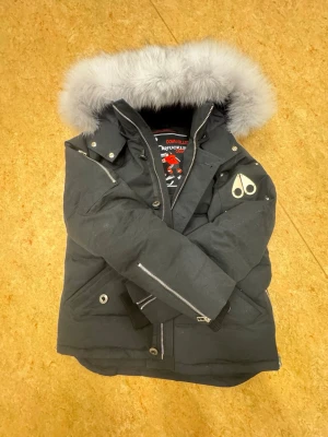 Svart dunjacka med pälskrage Moose Knuckles - Snygg svart dunjacka från Moose Knuckles med silverfärgade dragkedjor och detaljer. NFC funkar