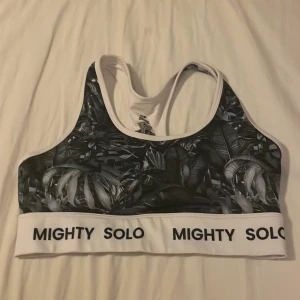 Set från Mighty Solo med tropiskt mönster - Snyggt loungewear-set från Mighty Solo med sport-bh och tights i svartvitt tropiskt blad-mönster. Båda plaggen har bred vit resår med logga. Perfekt för chill eller träning hemma. Materialet är stretchigt och bekvämt.