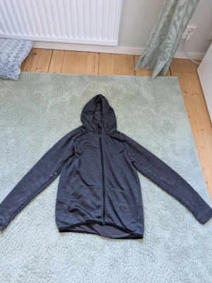 Mörkgrå sportig hoodie med dragkedja - Snygg mörkgrå hoodie med hel dragkedja framtill och huva. Tillverkad i ett mjukt, stretchigt funktionsmaterial som passar perfekt till träning eller chill.