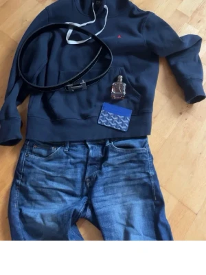 Mörkblå hoodie med liten logga - Snygg mörkblå hoodie från Polo Ralph Lauren med vit dragsko och liten röd logga på bröstet. Klassisk känguruficka framtill och mjukt material som känns skönt mot huden. Perfekt för en avslappnad och trendig stil.