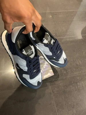 Valentino blåvita rockrunners - Snygga sneakers från Valentino i blått och vitt med mesh- och mockadetaljer. Skorna har svarta och vita inslag, grov sula och klassisk snörning. Märkeslogga på plösen och insidan. Perfekta för dig som vill ha en stilren och exklusiv look.