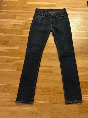 Mörkblå slim fit jeans från Nudie  - Snygga mörkblå jeans från Nudie Jeans i slim fit-modell. Klassisk femficksdesign med kontrastsömmar och knappgylf. Jeansen är tillverkade i ett mjukt denimtyg som ger en bekväm känsla och passar perfekt till en modern stil. Jeansen har en snygg fade och är i mycket bra skick. Bara höra av sig vid funderingar. Priset är inte fast tar emot bud.