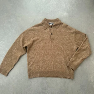 HOPE Brun stickad tröja med krage - Snygg brun stickad tröja från HOPE med klassisk krage och knäppning framtill. Tröjan har långa ärmar och är tillverkad i mjukt material, perfekt för en stilren och avslappnad look. Tröjan är sliten i designen (se kragen och muddarna). Köpt för någon månad sedan då original priset är 3600kr från HOPE (se bild 3). Aningen croppad och gjord av väldigt fint material. 