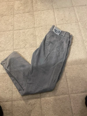 Gråa raka jeans från jocob Cohen  - Säljer ett par gråa jeans från Jacob Cohen  med rak passform och klassisk femficksdesign. Jeansen har en snygg logotyp-patch bak i midjan och är tillverkade i ett mjukt bomullsmaterial. Perfekta för en avslappnad och stilren look.