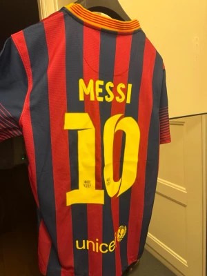 Barcelona Messi matchtröja Nike - Snygg Barcelona matchtröja med Messi och nummer 10 på ryggen. Tröjan har röda och blå vertikala ränder, gul Nike-logga och klubbmärke på bröstet samt Qatar Airways som sponsor. Tillverkad i lätt och ventilerande material, perfekt för fotboll eller träning.