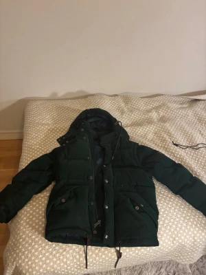 Mörkgrön dunjacka/ Manchester jacka från Polo Ralph Lauren - Säljer en mörkgrön dunjacka från Polo Ralph Lauren med huva och stora framfickor. Jackan är tillverkad i manchestertyg och har snygga detaljer som läderpatch på ärmen. Perfekt för kalla vinterdagar och riktigt stilren. Den har en inbyggd väst, vilket man får bara genom att ta av ärmarna, säljer pga för stor. Köpte ny för 8000kr. Alltid öppen för frågor! 