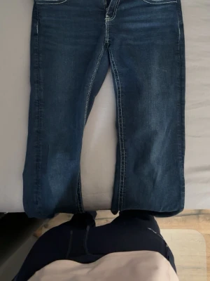 Mörkblå jeans lågmidja - Snygga mörkblå jeans långmidjade med vita kontrastsömmar från Gina i storlek 170. Bakfickorna har lock och knappdetaljer. Inuti en av fickorna finns en sminkfläck men den är inte synlig när man har på sig de. Jeansen har rak passform och är tillverkade i denim. Står för frakten!💖
