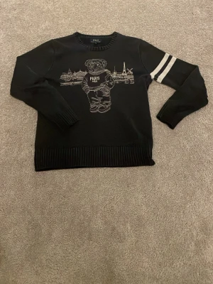 Svart stickad tröja Polo Bear Paris - Stickad tröja från Polo Ralph Lauren med Polo Bear och Paris-motiv framtill. 