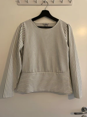 Vit och svart randig blus  - Snygg vit blus med svarta vertikala ränder. Modellen har rund halsringning, långa ärmar och en bredare randig panel nedtill som ger en cool kontrast. Perfekt att styla med jeans eller kjol för en trendig look.