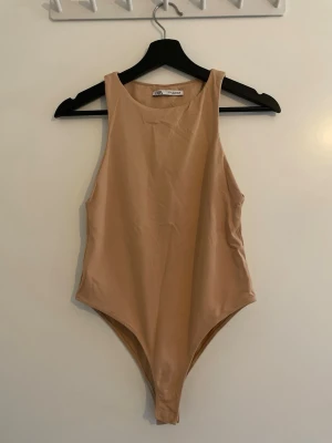 Beige body från Zara - Snygg beige body från Zara med hög halsringning och klassisk, stilren design. Tillverkad i mjukt och stretchigt material som sitter skönt mot kroppen. Perfekt att styla till olika outfits för en clean look.