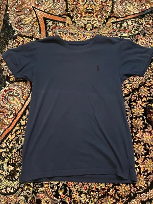 Mörkblå t-shirt från Polo Ralph Lauren - Snygg mörkblå t-shirt från Polo Ralph Lauren i regular fit. Klassisk design med rund halsringning och diskret broderad logga på bröstet. Tillverkad i 100% bomull för en skön och mjuk känsla. Perfekt till jeans eller shorts.