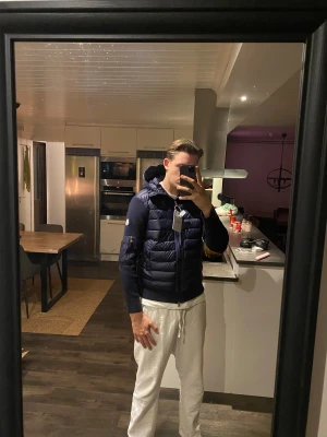 Mörkblå Moncler pufferjacka med huva - Säljer en snygg mörkblå cardigan från Moncler med stickade ärmar och huva. Jackan har quiltad framsida, dragkedja, ribbade muddar och en ficka med dragkedja på ärmen. Ikonisk Moncler-logga på vänster ärm. Perfekt för dig som vill ha en clean och exklusiv look.             Är 187cm på bilden!