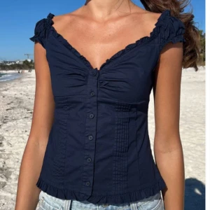 Super populär topp från brandy Melville! - Supersöt mörkblå blus med v-ringad hals och volangdetaljer längs kanterna. Blusen har korta ärmar, knappar hela vägen framtill och rynkade partier vid bysten. OBS: lånade bilder men kan skicka egna vid intresse! 