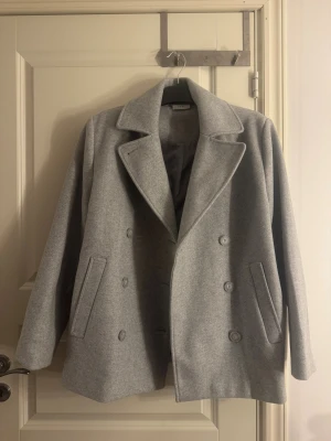 Grå skepparkavaj från Zara - Säljer en stilren och helt ny grå skeppkappa med klassisk dubbelknäppning och breda slag. Kappan har två sidofickor och är tillverkad i mjukt ullmaterial som ger en clean och modern look. Den är verkligen super ny med prislappen på. 