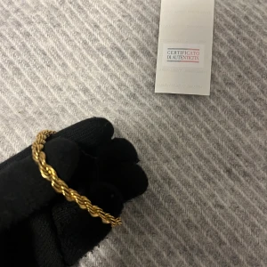 18K Guldarmband från Giorgio Armani - Snyggt guldarmband från Giorgio Armani med certifikat. Armbandet har en tvinnad kedja och ett stilrent lås i guldfärgad metall. Perfekt för dig som vill ha en exklusiv och trendig accessoar med lyxig känsla.