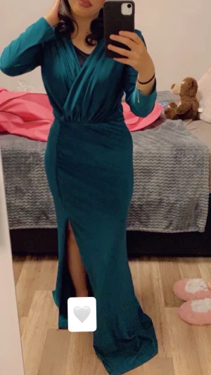 Festklänning med slits - Säljer en supersnygg långklänning i en djup petrolgrön färg. Den har en smickrande omlottdesign upptill, markerad midja och en stilren slits framtill som ger en elegant men ändå chic look. Skönt stretchigt material som sitter fint på kroppen utan att kännas tight.