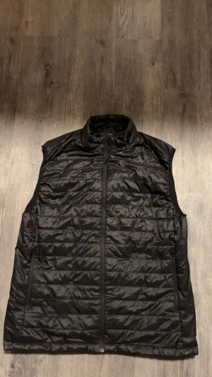 Svart puffer-väst från H&M, storlek L - Svart puffer-väst från H&M i storlek L. Västen har quiltad design, hög krage och dragkedja framtill. Finns två fickor på utsidan och en på insidan. Tillverkad i 100% polyester, perfekt för lager-på-lager under kyliga dagar. Snygg och enkel att matcha med hoodies eller tröjor.