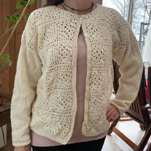 Beige stickad kofta med virkade detaljer - Superfin beige kofta med virkade rutor fram och slät stickade ärmar och rygg. Koftan har rund hals, pärlemorknappar och ett luftigt, unikt mönster framtill. Mjuk och skön. Perfekt för lager-på-lager och ger en chill vintagevibe till din outfit. Helt ny och inte använd, blev lite för stor för mig. Uppskattas som en L