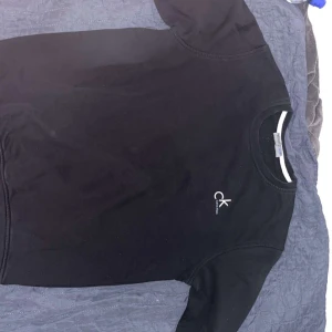 Svart t-shirt från Calvin Klein - Snygg svart t-shirt från Calvin Klein med klassisk rund hals och diskret CK-logga på bröstet. T-shirten har korta ärmar och är gjord i mjuk bomull som känns skön mot huden. Perfekt för dig som gillar stilrena och enkla plagg.