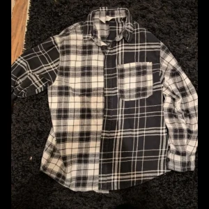 Svartvit rutig skjorta från H&M stl 146 - Säljer en svartvit rutig skjorta från H&M i bomull. Skjortan har klassisk krage, bröstficka och knäppning framtill. Snygg kontrast mellan svart och vit på vardera sida, vilket ger en cool look. Perfekt för dig som gillar streetstyle.