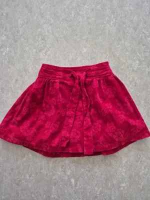 Kjol - Snygg röd kjol från FIX med blommigt mönster och mjukt manchestertyg. Kjolen har ett knytband i midjan och volangig tyll på insidan för extra fluff. Perfekt för dig som gillar färg och detaljer! 