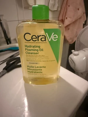 CeraVe Hydrating Foaming Oil Cleanser - Stor flaska med CeraVe Hydrating Foaming Oil Cleanser, perfekt för normal till mycket torr hud. Oljebaserad rengöring som är parfymfri och innehåller ceramider, triglycerider och squalane. Flaskan är transparent med grön etikett och grön kork. Endast testad se bilderna.